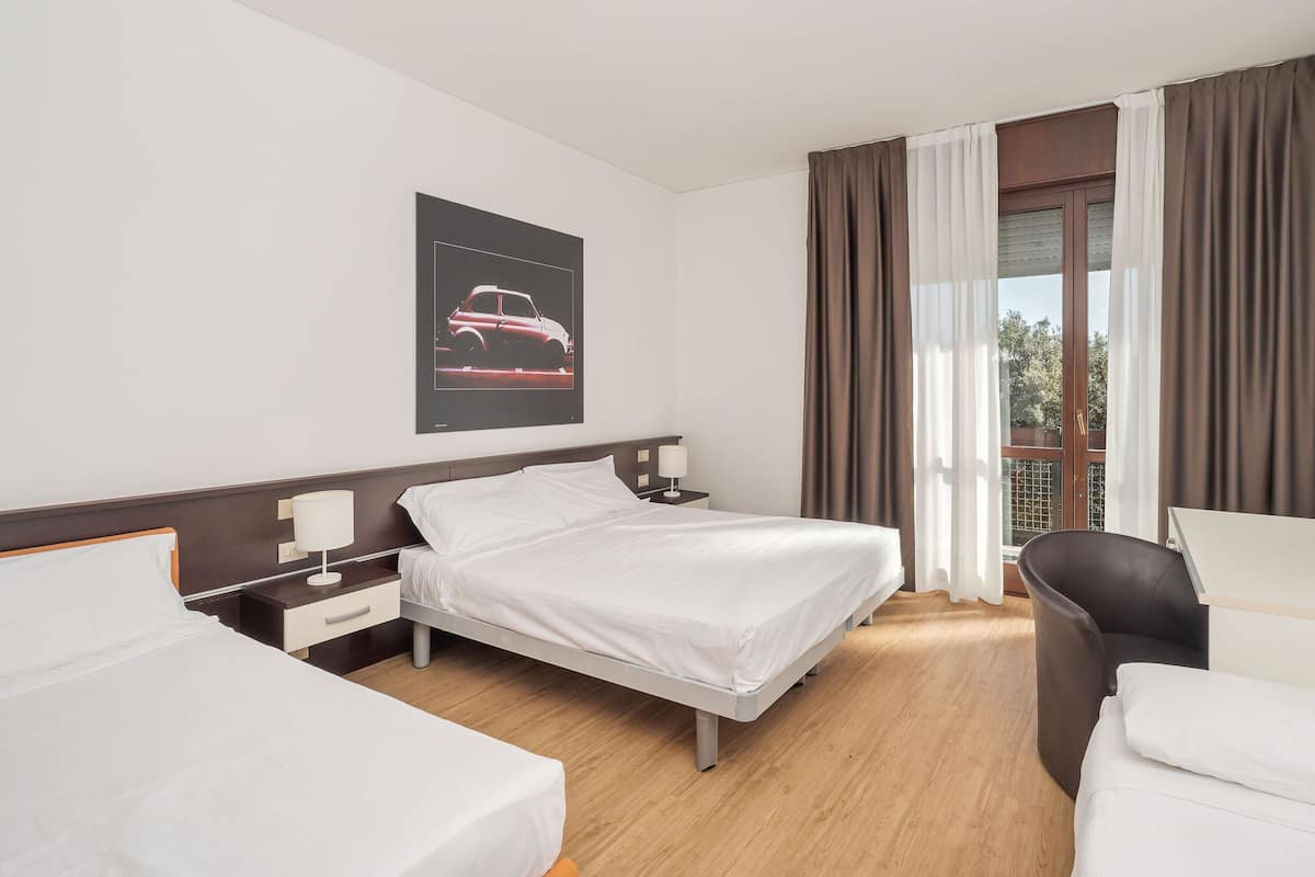 A hotel room with two beds, a desk, a chair, and a large window with curtains.