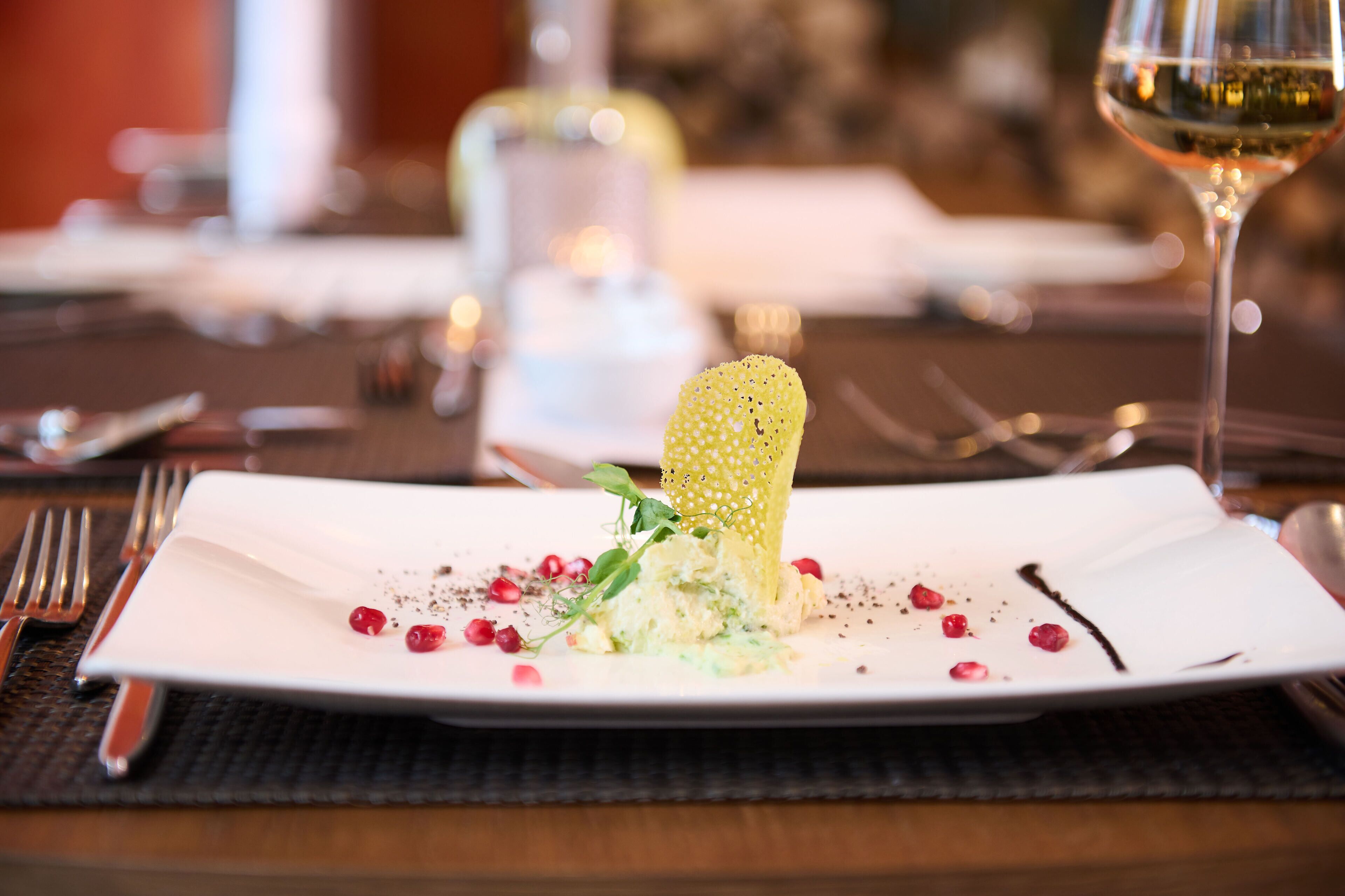 A white plate with a unique food presentation, including a crispy element and garnishes, on a dark tablecloth.