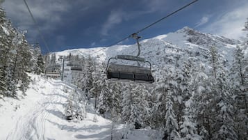 Una seggiovia in una zona montana innevata, con alberi e cielo sereno.
