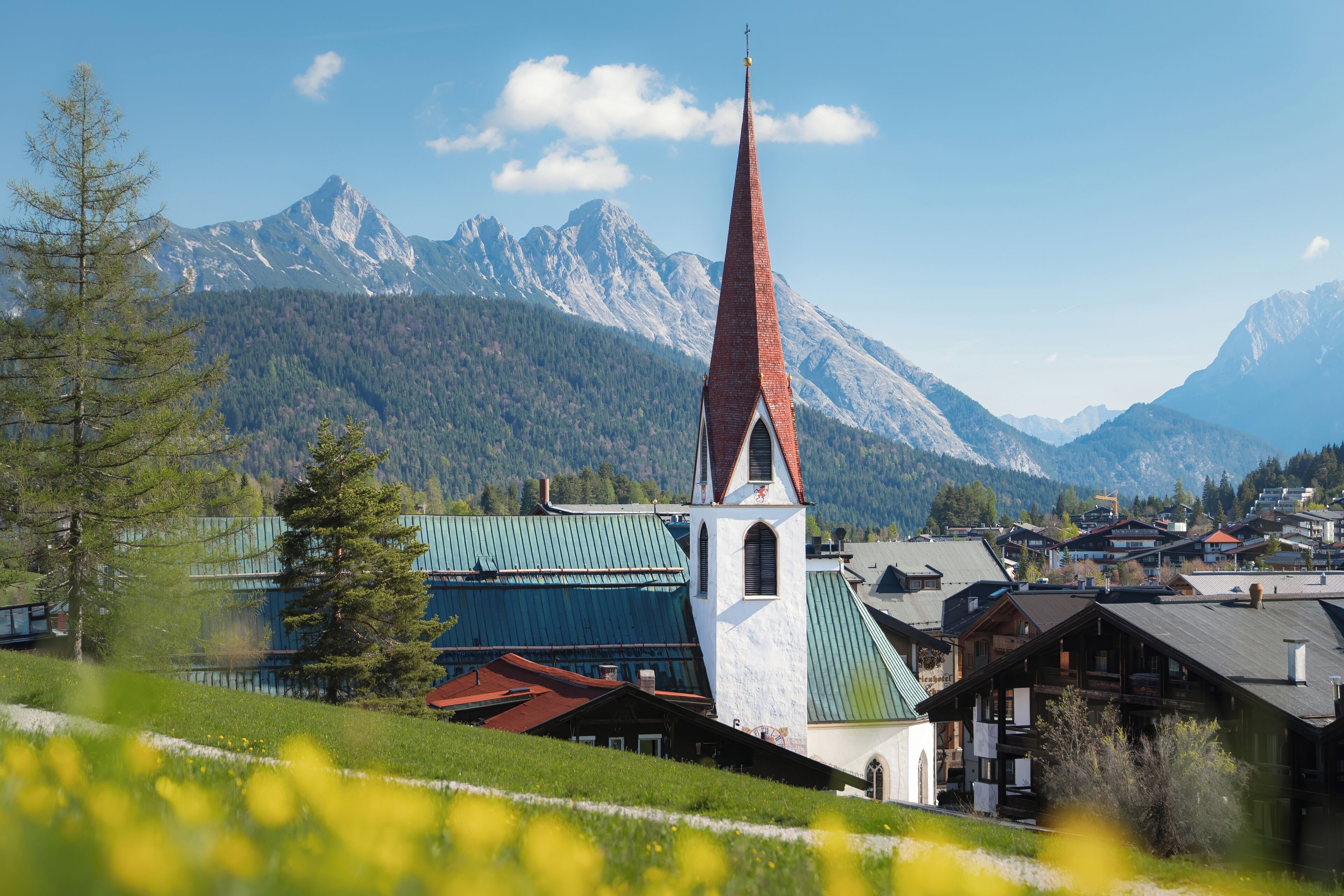 A church with a tall spire, surrounded by a village with traditional houses and a mountain backdrop.