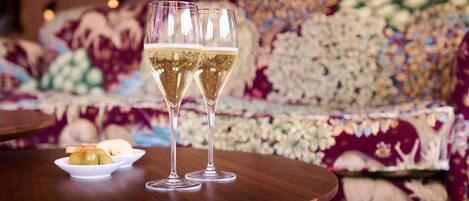 Two glasses of champagne on a wooden table with a floral sofa in the background.