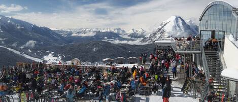 A crowded outdoor seating area with snow-covered mountains in the background.