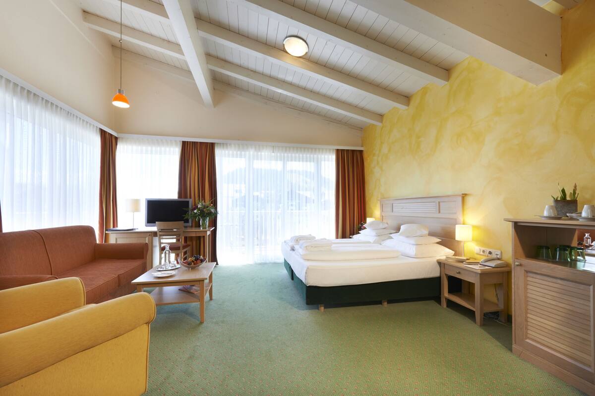 A hotel room with a bed, a sofa, a desk, a television, and a window with curtains.