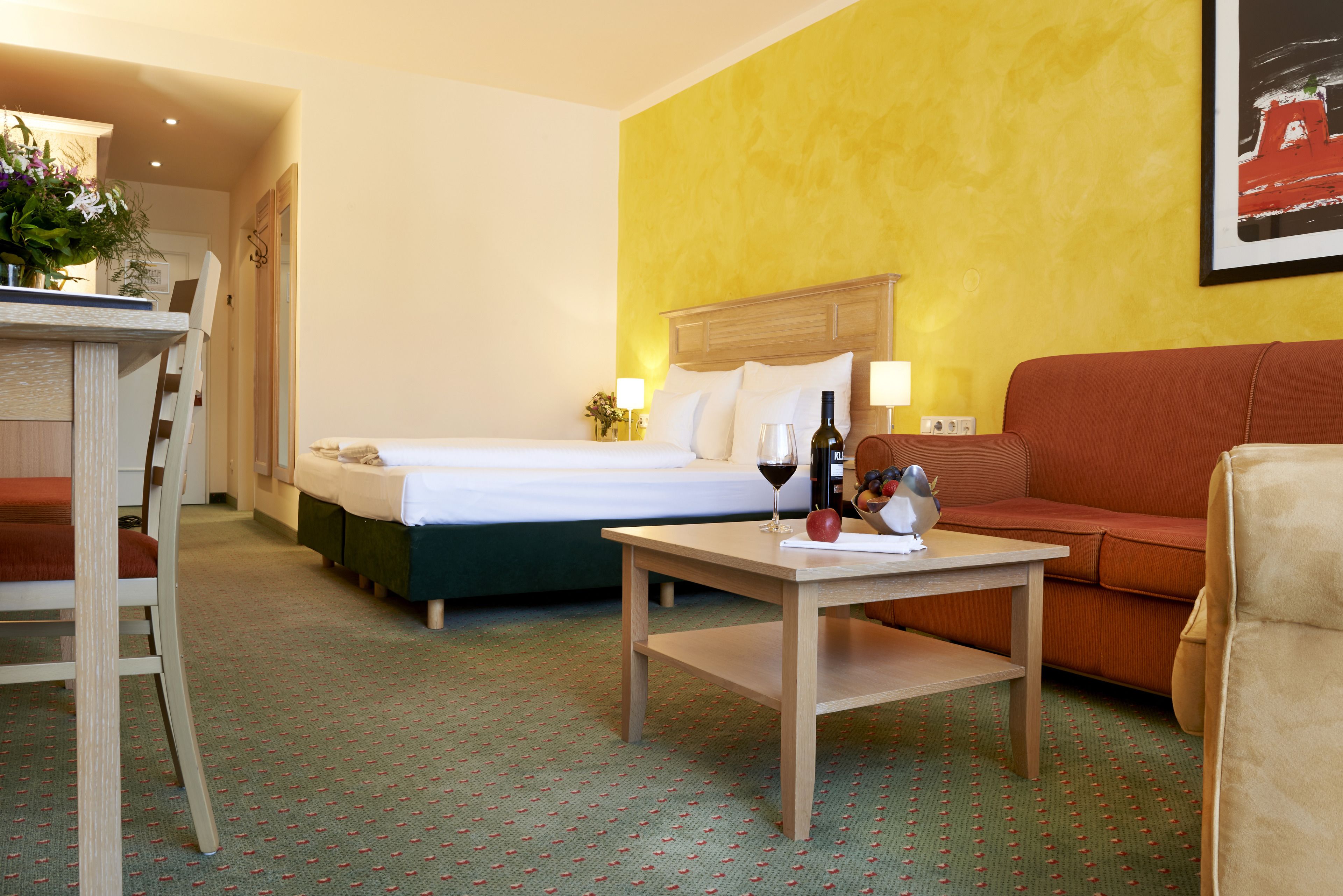 Habitación de hotel con una cama, una mesa con una botella de vino y una manzana, un sofá y una silla.