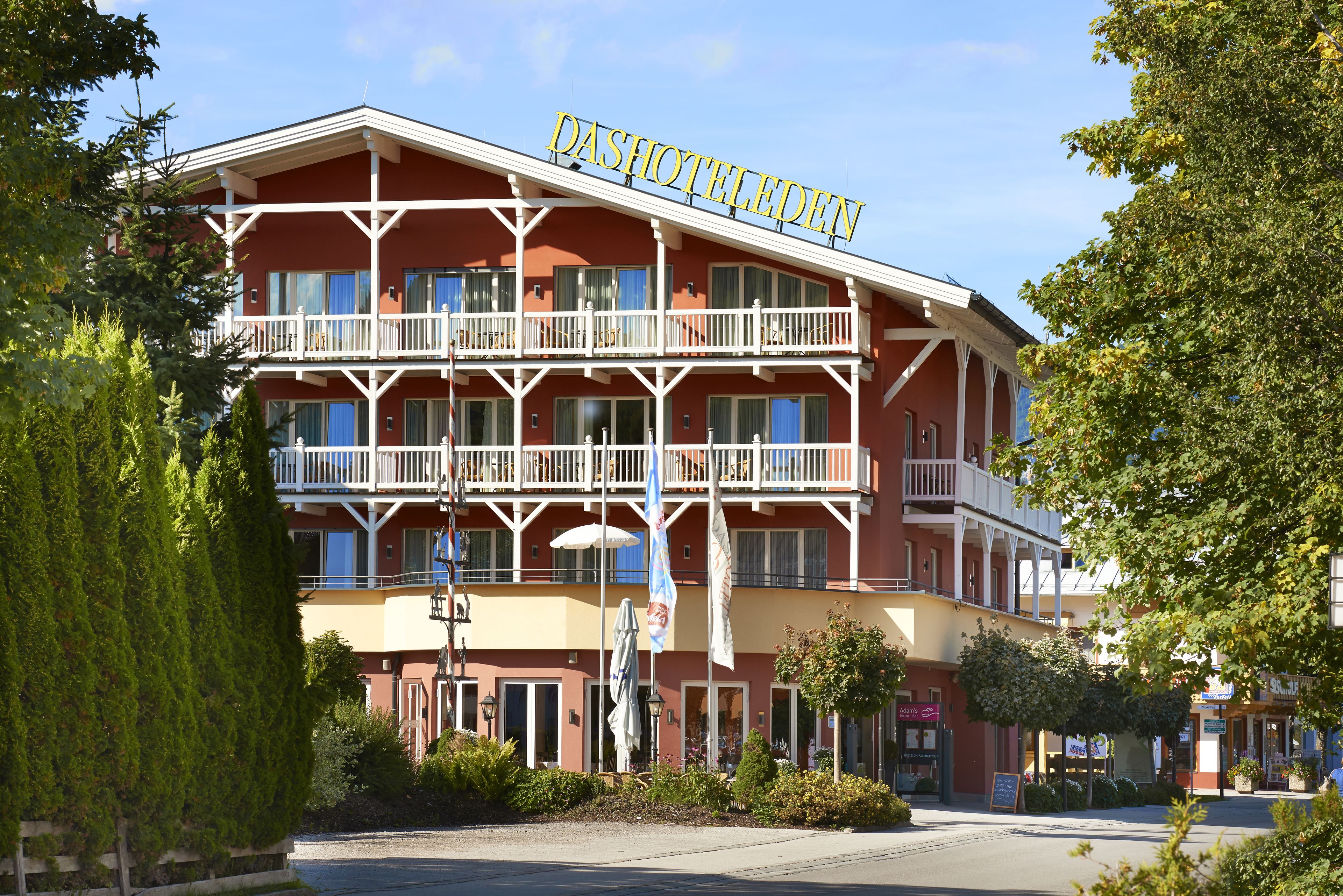 A multi-story hotel with balconies, a sign reading "DASHOTELEDEHN," and a street view with shops and greenery.