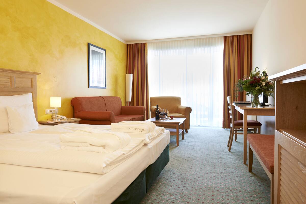 A hotel room with a large bed, a desk, a chair, and a sofa.