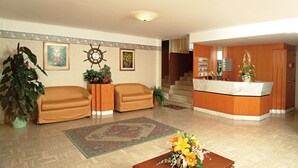 Un hall d’hôtel comprenant un comptoir d’accueil, deux canapés, une table basse ornée de fleurs, une grande plante et un tapis à motifs.