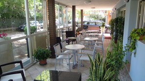 Un espace café en plein air avec des tables et des chaises, des plantes en pot et une vue sur la rue.