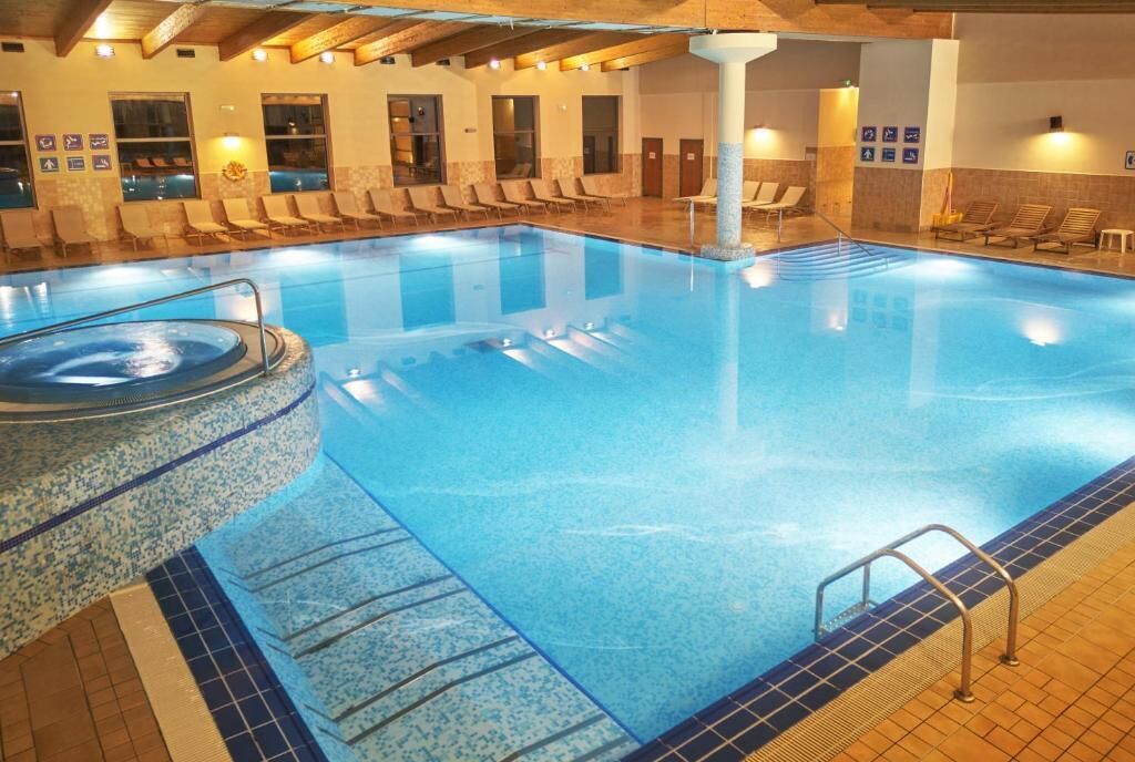 A large indoor swimming pool with a hot tub, lounge chairs, and a tiled floor.