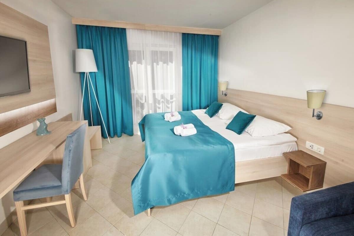 A hotel room with a bed, a desk, a chair, a TV, and a window with curtains.