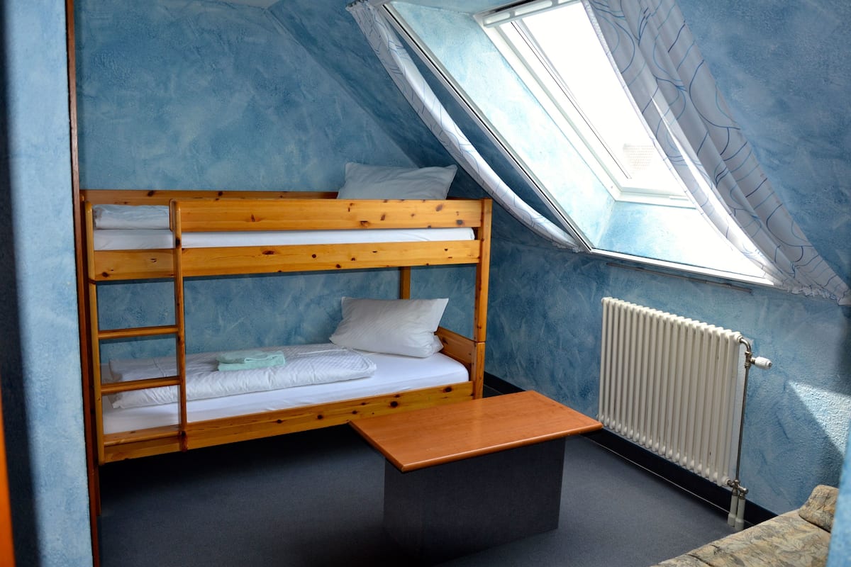 A bunk bed with a wooden frame and white bedding, a small wooden table, and a radiator.