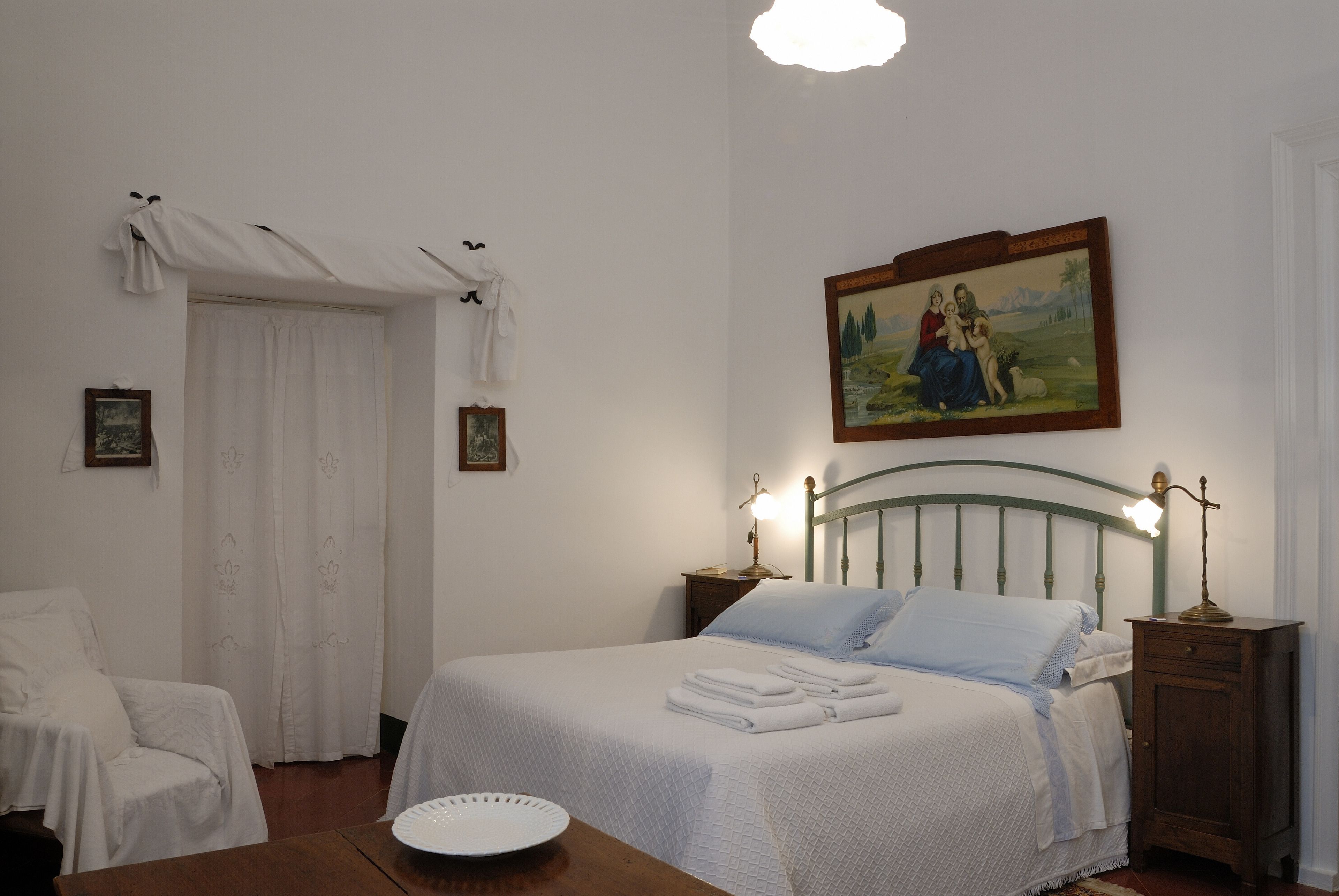 Een netjes opgemaakt slaapkamer met een bed, nachtkastje, stoel en een schilderij aan de muur.
