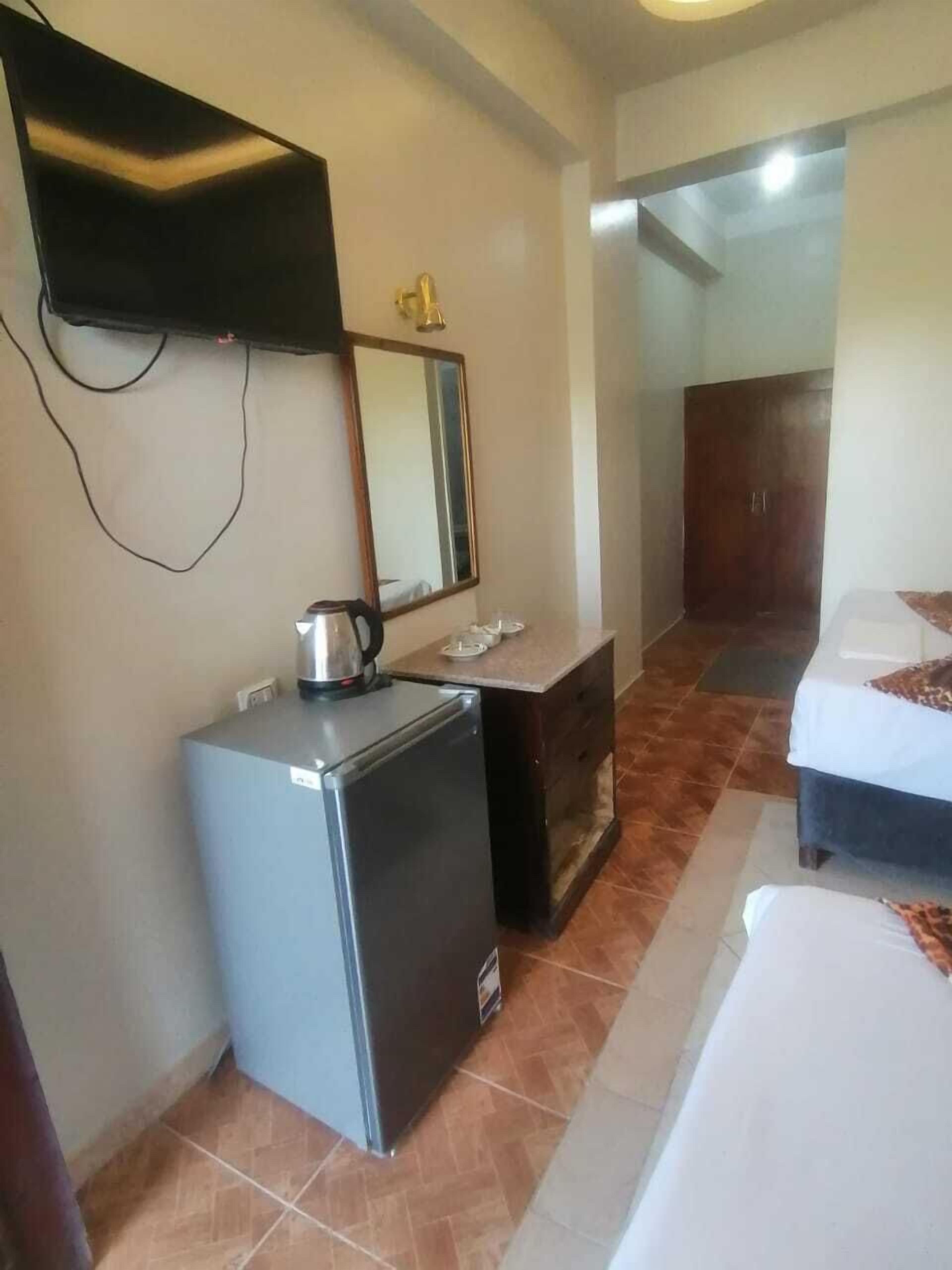A compact hotel room with a small kitchenette, a bed, a wardrobe, and a television mounted on the wall.