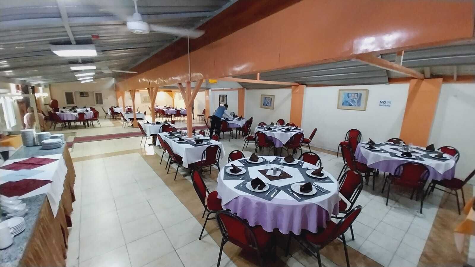 A dining hall with multiple round tables covered with white tablecloths and red chairs.