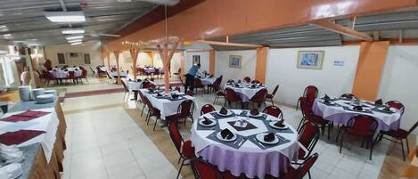 A dining hall with multiple round tables covered with white tablecloths and red chairs.