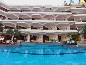 Ein mehrstöckiges Hotel mit einem Schwimmbecken im Vordergrund.