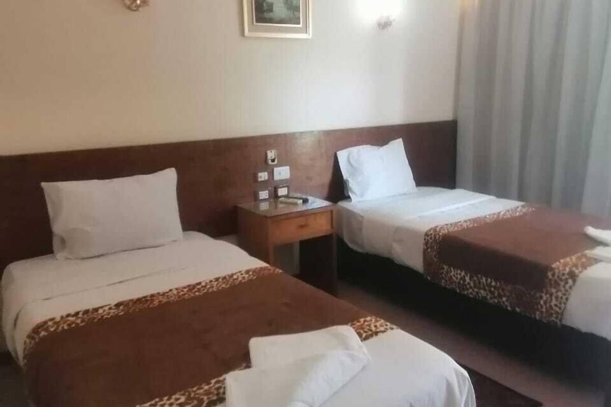 Una habitación de hotel con dos camas, una mesita de noche, una lámpara de pared y una ventana con cortinas.