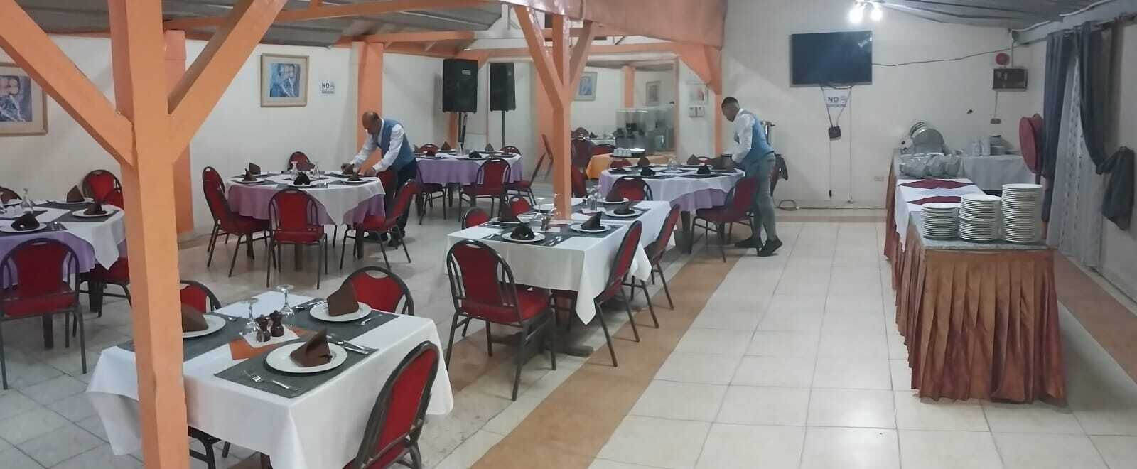 Une salle à manger avec des tables dressées pour les repas, du personnel aux petits soins pour les clients et un espace buffet où les assiettes sont empilées.