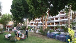 An outdoor seating area with tables and chairs, surrounded by trees and a building with multiple balconies. - Rezeiky Hotel And Camp Luxor (Luxor)