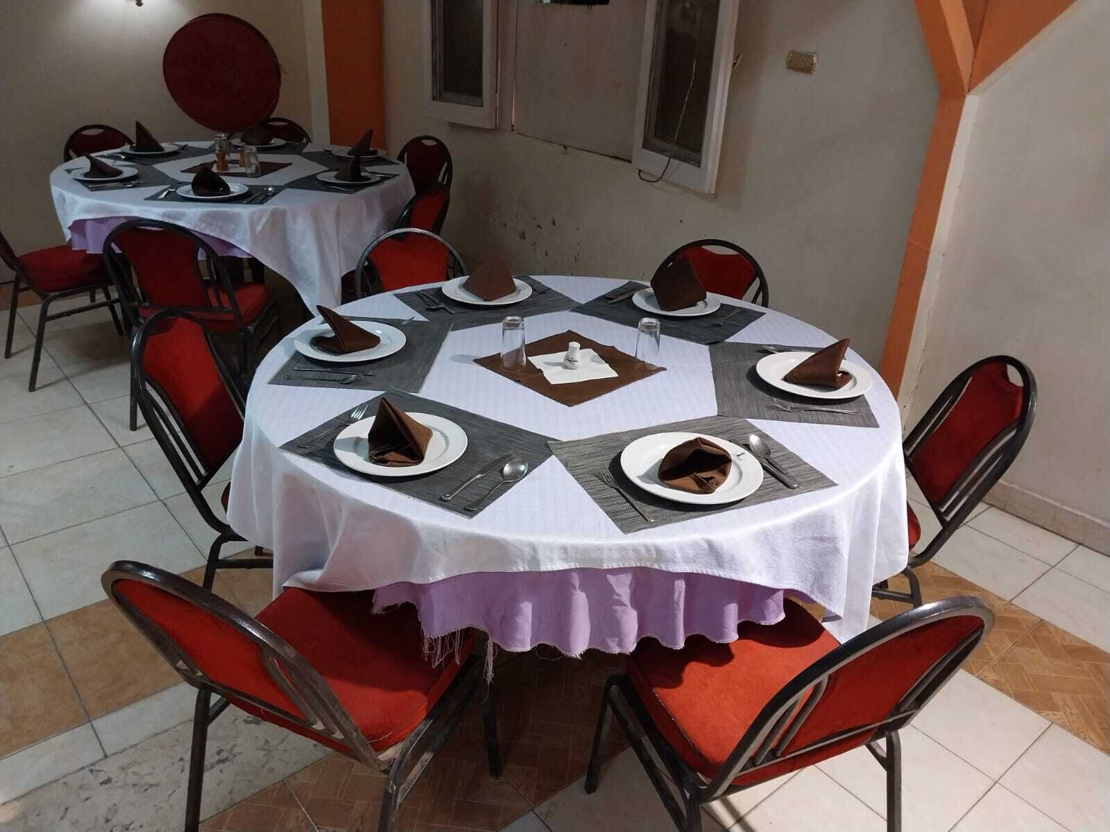A dining area with round tables, red chairs, and white tablecloths.