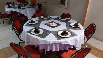 A dining area with round tables, red chairs, and white tablecloths.