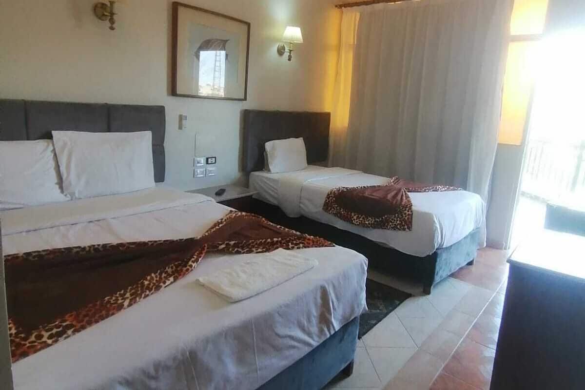 Habitación de hotel con dos camas, un ventilador de techo, un equipo de aire acondicionado, una lámpara de noche y una ventana con cortinas.