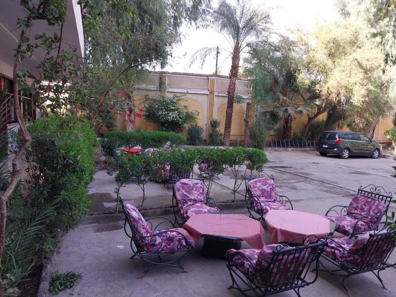 Eine Terrasse im Freien mit einem runden Tisch und sechs Stühlen, umgeben von Grünpflanzen und einer gelben Wand.