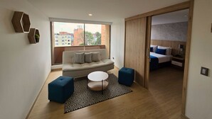 A modern living room with a sofa, ottomans, a coffee table, and a patterned rug. - Hotel Confort 80 Zona Rosa (Bogotá)