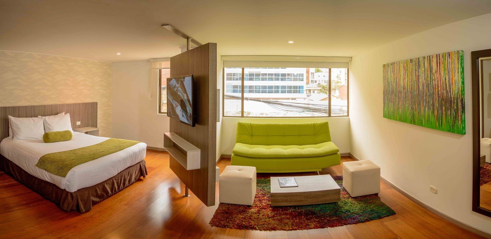 A modern hotel room with a bed, a green sofa, a TV, and a large window.