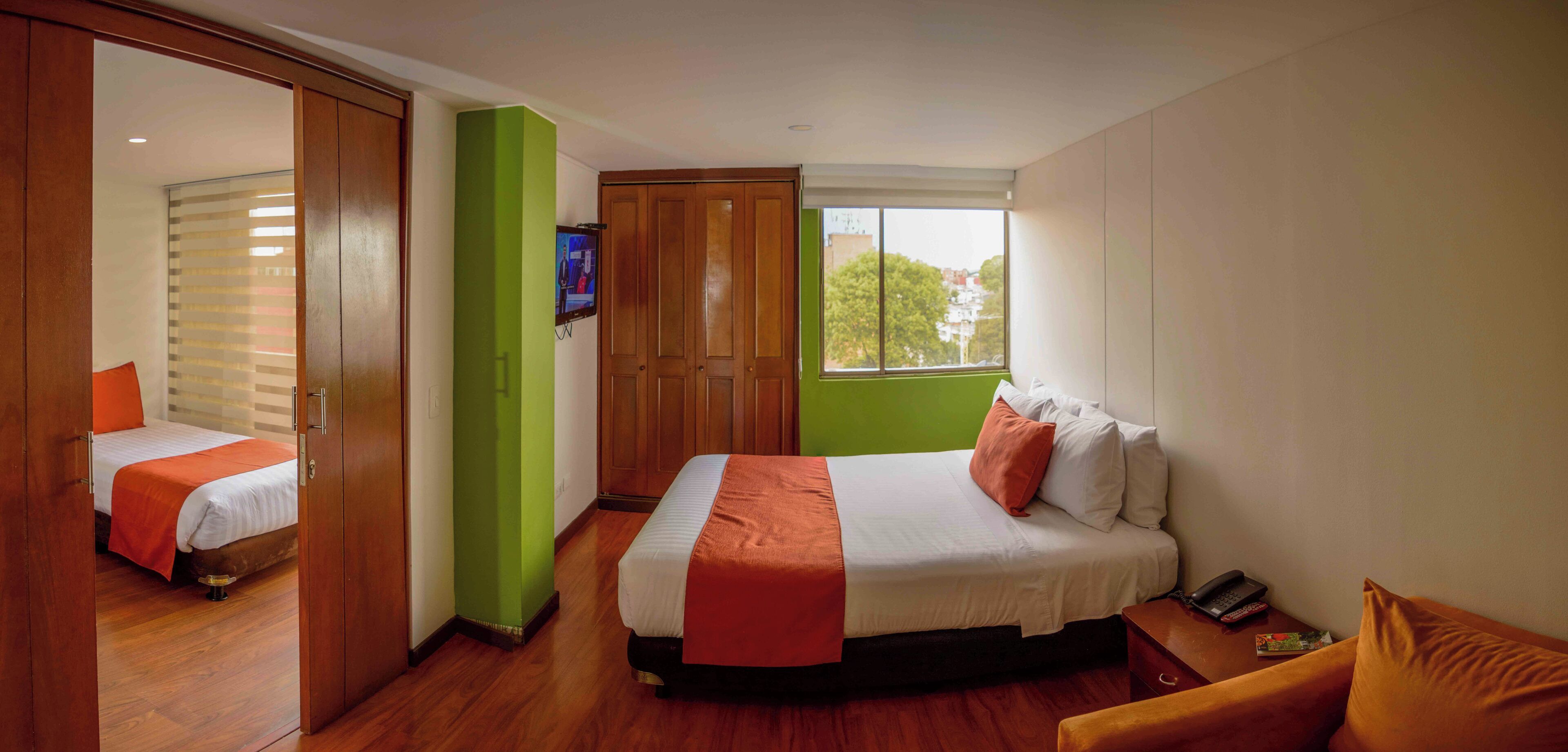 A hotel room with two beds, a TV, a window, and a wooden floor.