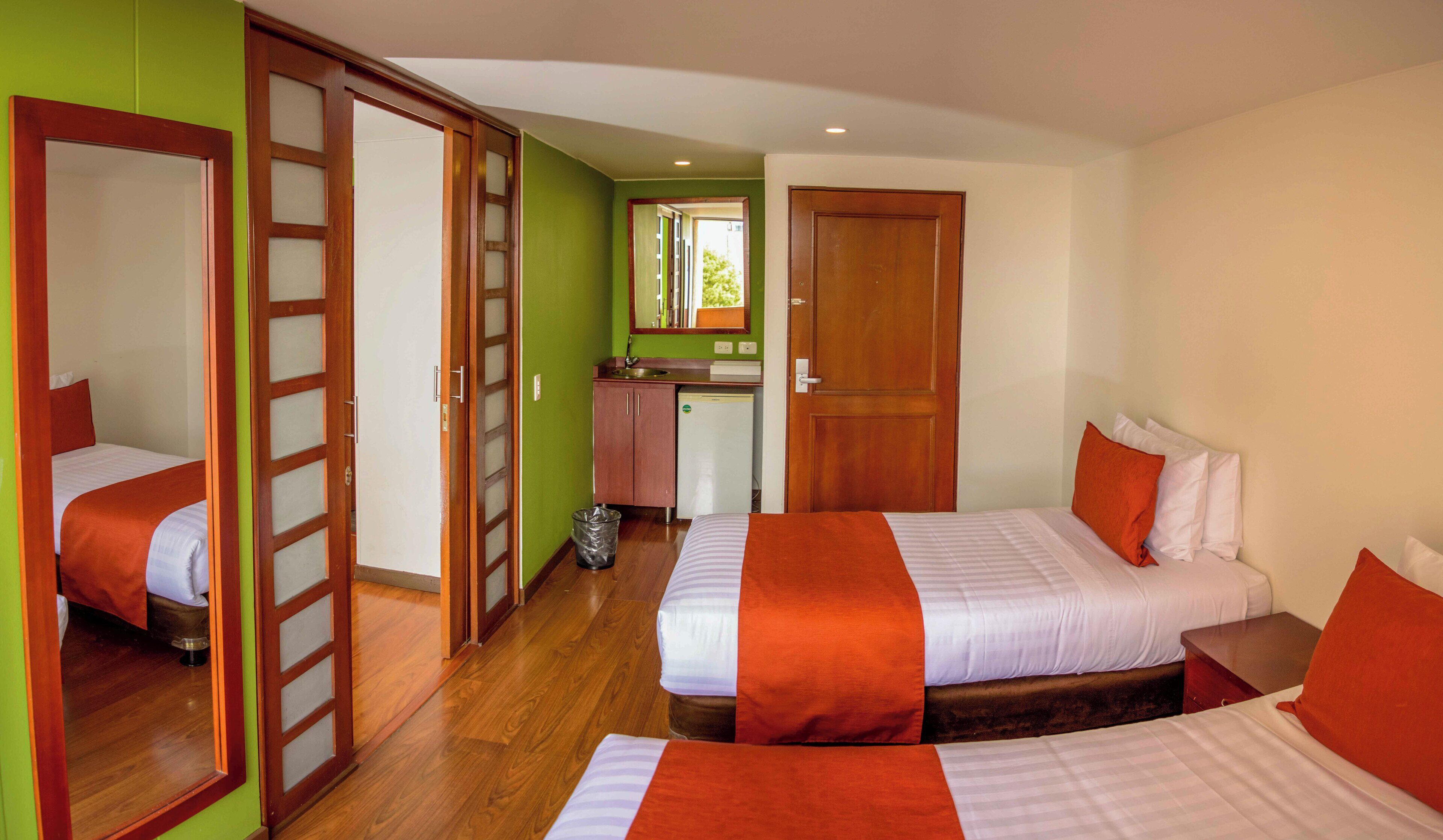 Quarto de hotel com duas camas, banheiro e cozinha compacta.