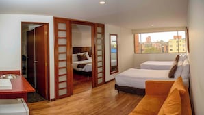 A hotel room with a wooden floor, a bed, a sofa, a desk, and a window with a city view. - Hotel Confort 80 Zona Rosa (Bogotá)