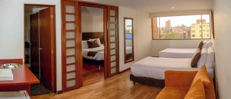 Een hotelkamer met een houten vloer, een bed, een bank, een bureau en een raam met uitzicht op de stad.