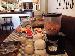 Una barra de desayuno con diversas opciones de comida, una máquina de café y un gran recipiente con cereales.