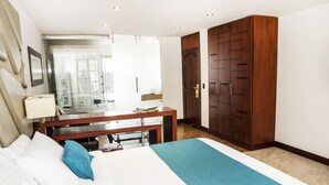 Habitación de hotel con cama, escritorio, armario y baño visible a través de una puerta de cristal.