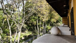 Vista de un edificio con balcón de hormigón que da a un jardín con árboles y un camino.