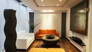 Una sala de estar moderna con un sofá blanco, un sofá naranja, una mesa de centro redonda y una gran escultura abstracta.