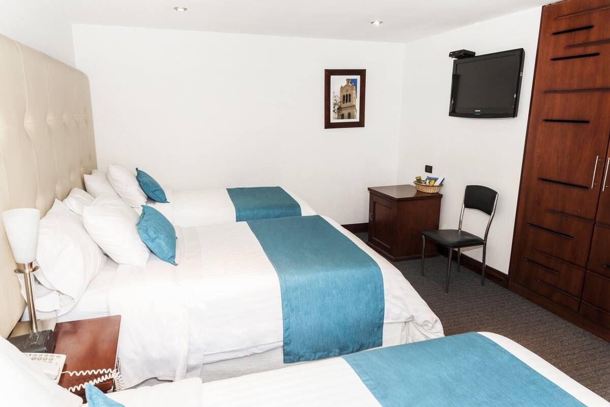 Una habitación de hotel con dos camas, un escritorio, una silla, un televisor y un armario.