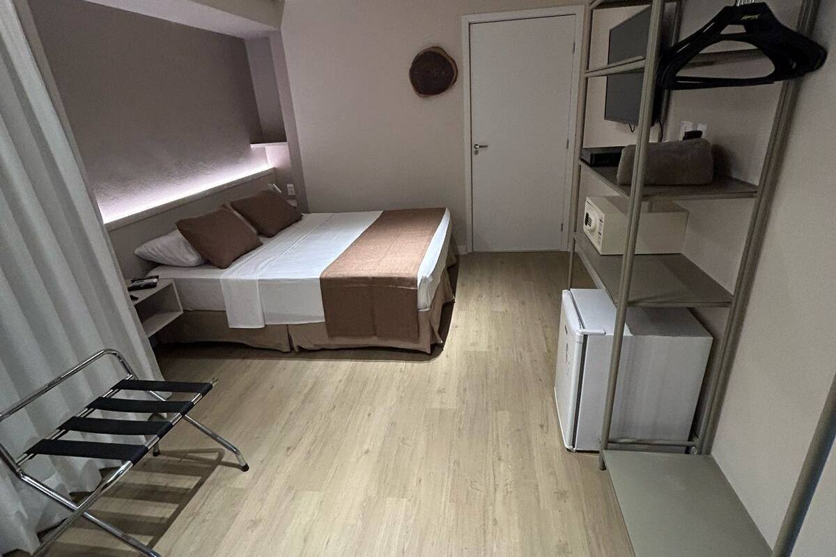 A compact bedroom with a bunk bed, a small desk, a wardrobe, and a hanging rack.