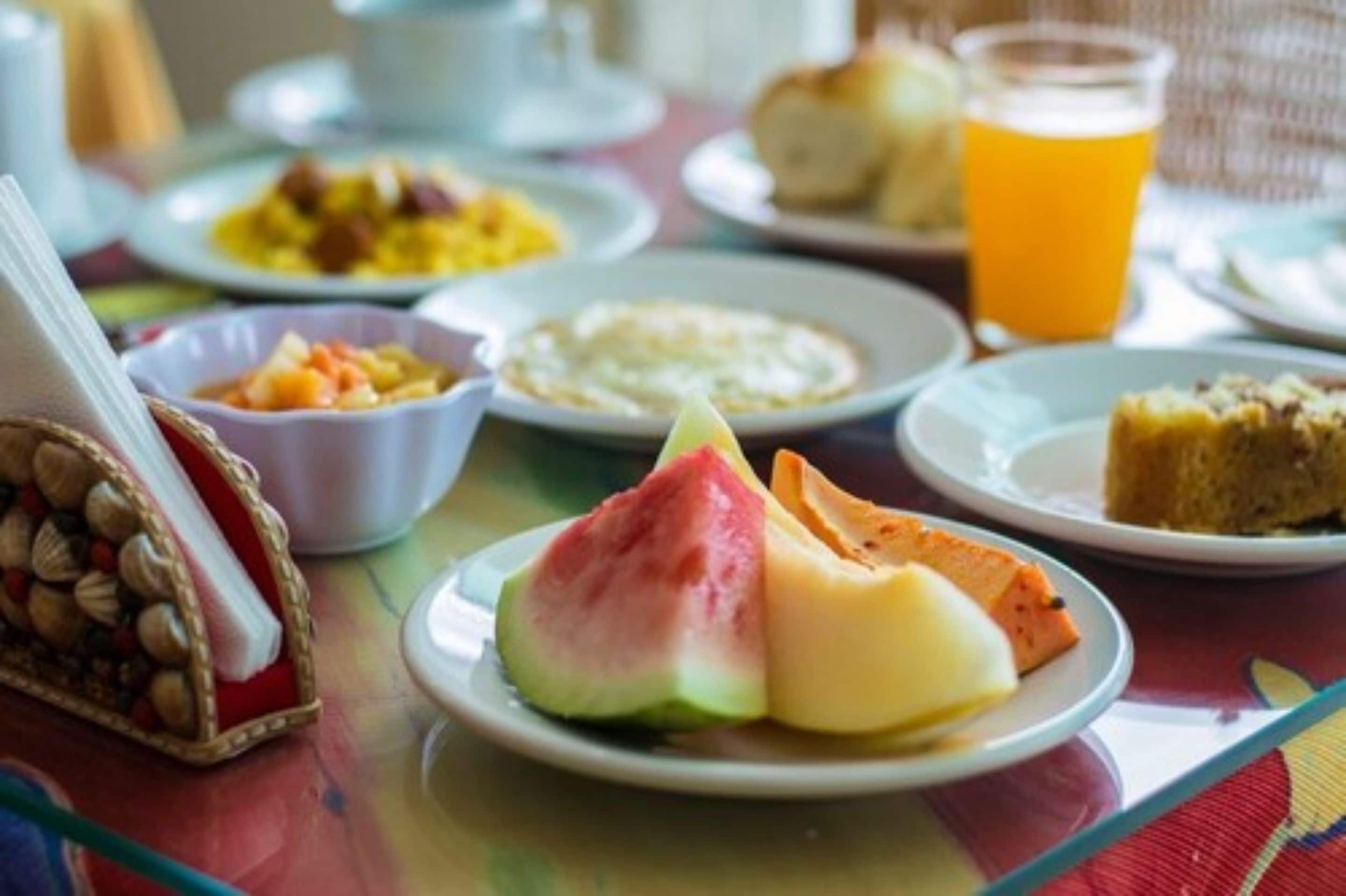 Een ontbijttafel met diverse gerechten, waaronder een bord met watermeloen en kaas, een fruitschaal en een glas sinaasappelsap.