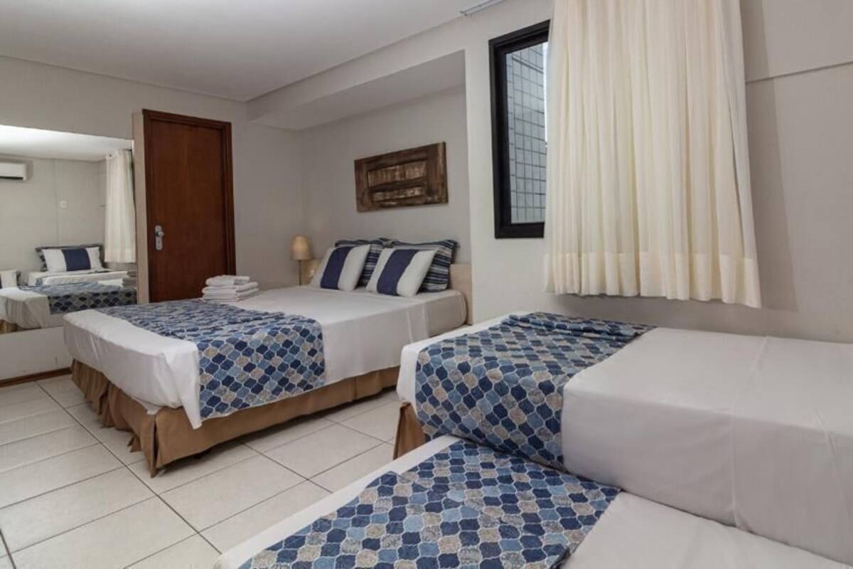A hotel room with two beds, a window with curtains, a wooden door, and a wall-mounted artwork.