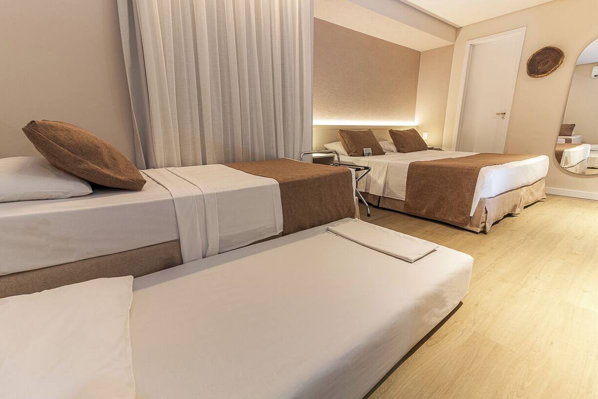 A hotel room with two single beds, a bedside table, a chair, a mirror, and a door.