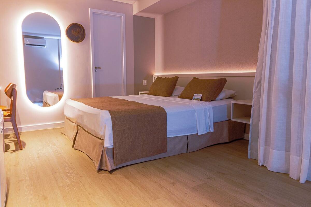 A bedroom with a large bed, a bedside table, a chair, a mirror, and a door.