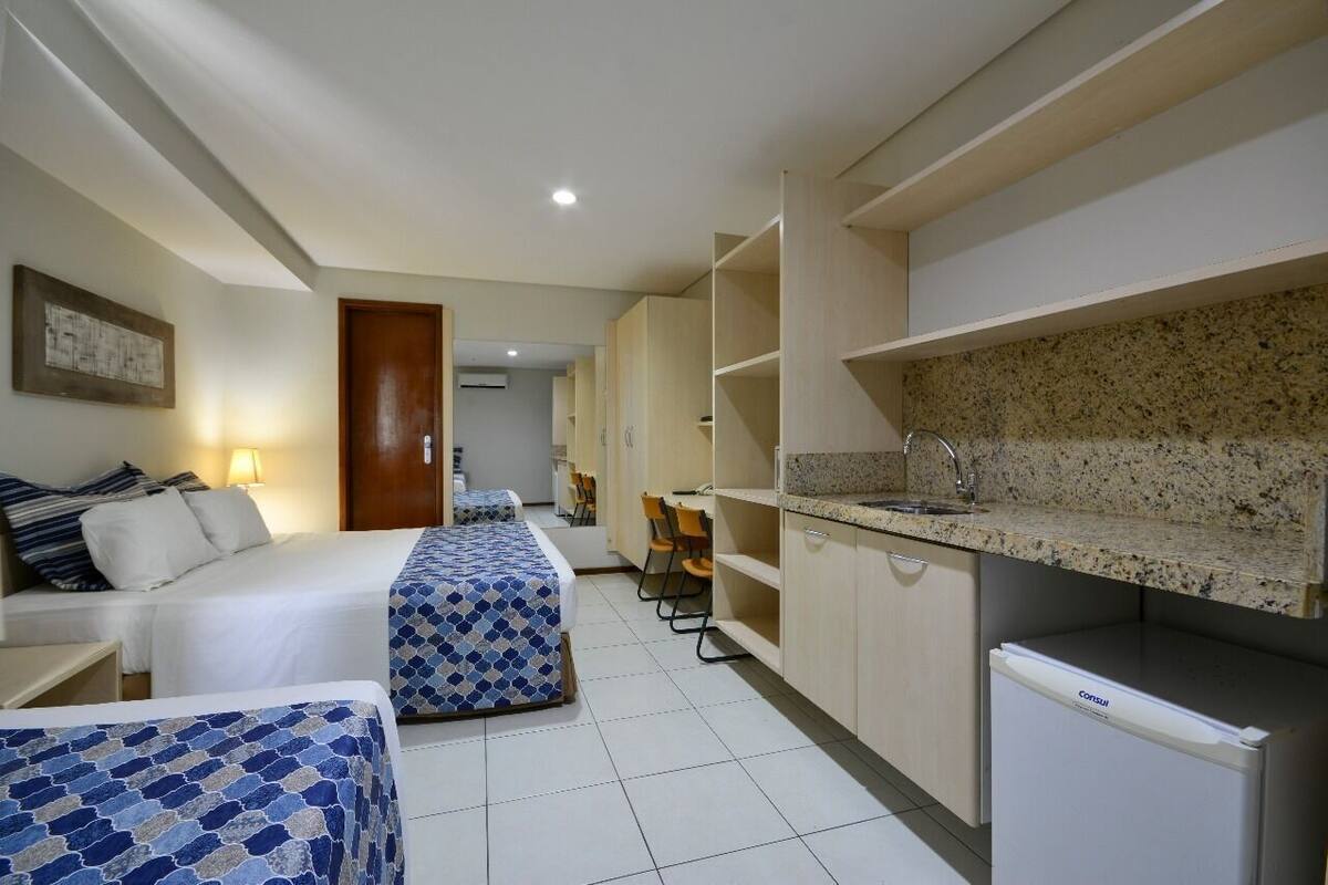 A hotel room with a bed, a desk, a kitchenette, and a bathroom.