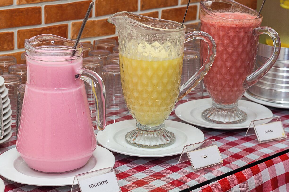 Trois carafes contenant des boissons de couleurs différentes sont posées sur une nappe à carreaux, et chaque boisson est accompagnée d’une étiquette indiquant son nom.