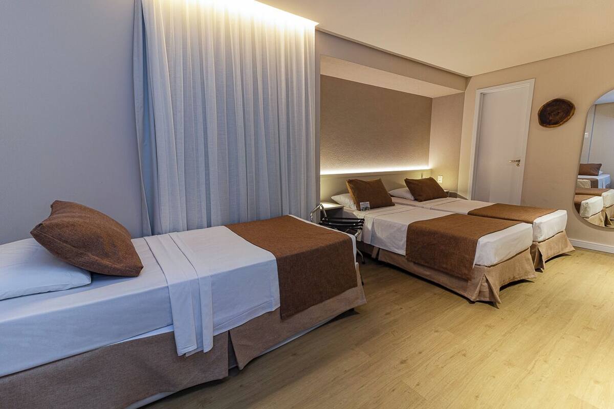 A hotel room with two beds, a bedside table with a lamp, a mirror, and a door.