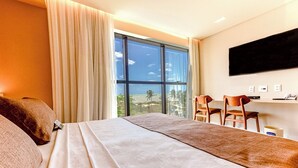 Habitación de hotel con una cama grande, un televisor montado en la pared y vistas a la playa desde la ventana.