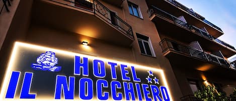 A hotel sign with illuminated blue letters spelling "HOTEL IL NOCCIERO" against a building facade.
