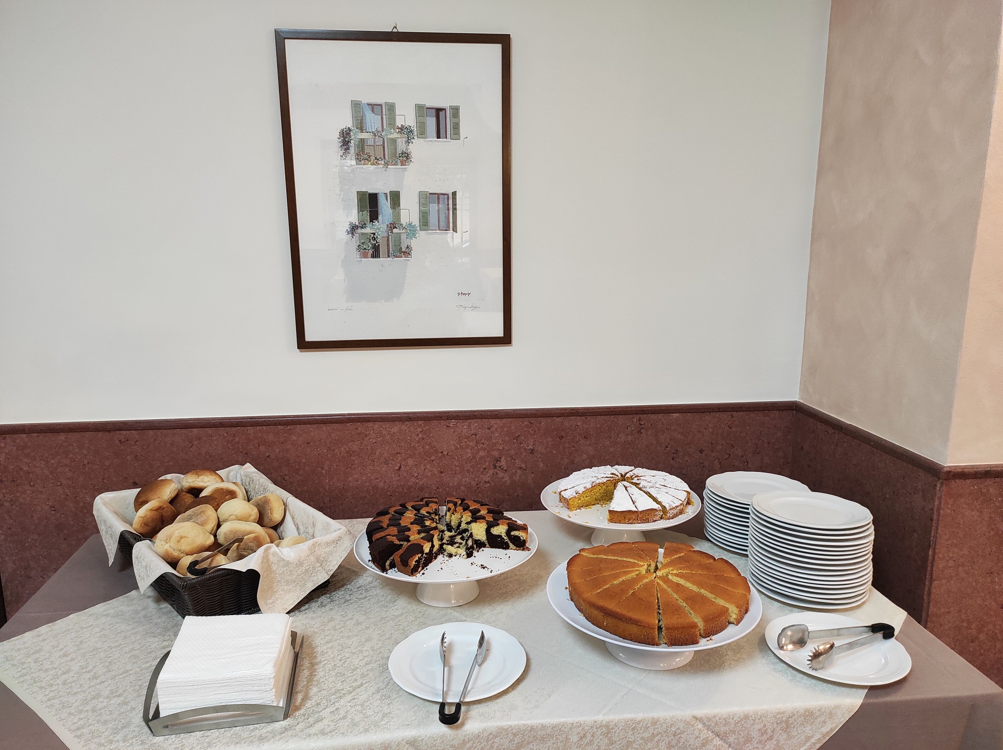 A table with various baked goods, including bread and cakes, and a framed picture on the wall.