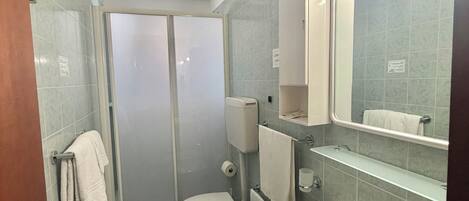 Un baño con inodoro, bidé y lavamanos, un espejo con iluminación y zona de ducha.